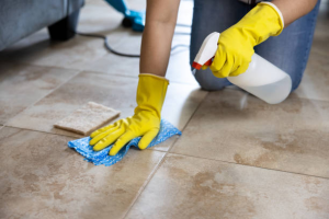 Person wearing yellow gloves scrubbing tile floor with spray during Grout Cleaning.