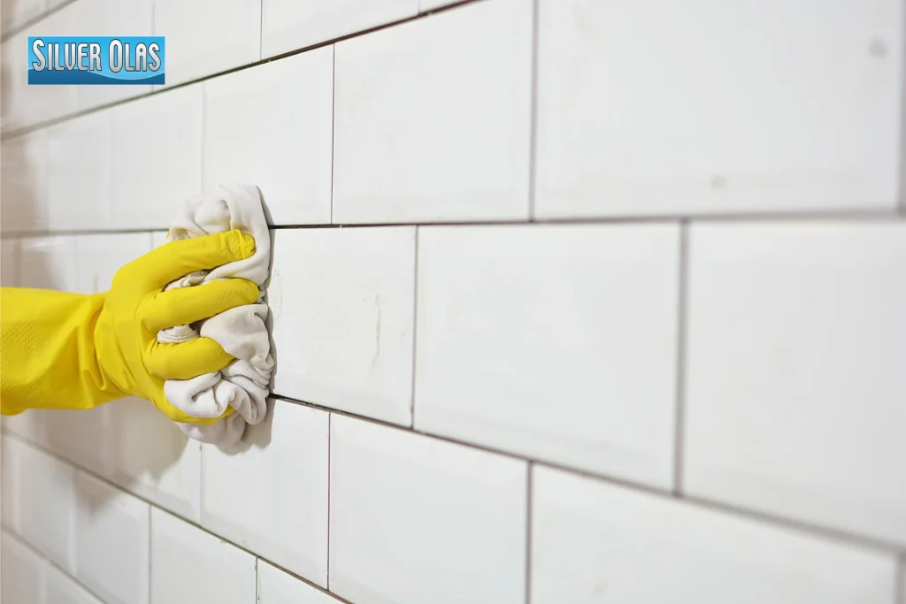 Person wearing yellow gloves wiping white tile surface for grout cleaning vs regrouting.