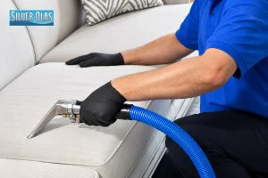 Technician vacuuming light fabric sofa cushion for professional upholstery cleaning.